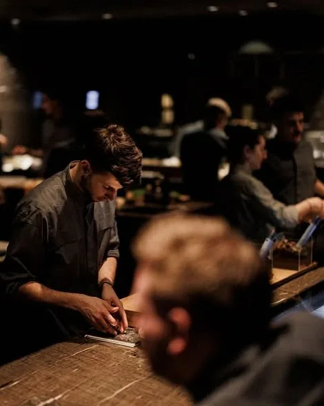 An Alchemist chef finishing a course with tweezers under low warm light
